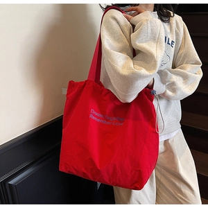 Detail of red canvas tote bag with drawstring and blue Dream Together text on model