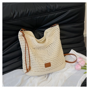 Detailed view of beige hollow woven tote bag with brown leather tag and long shoulder strap