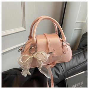 Detailed side view of pink bow shell handbag with pearl pendant and pearlescent leather