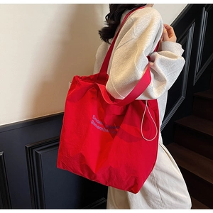 Close-up of a large red canvas tote bag featuring blue artistic letter print design