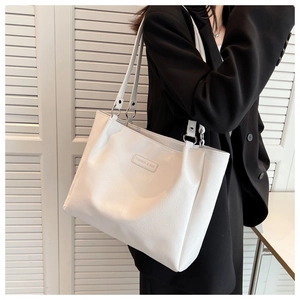 Close-up of a white lychee grain leather tote bag with long straps on a model in a black suit