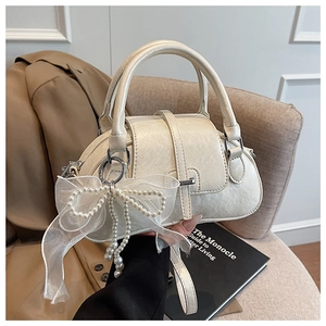 Detailed shot of textured cream leather handbag with pearl bow charm and silver hardware