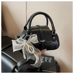 Detail of black glossy wrinkled handbag with pearl lace bow charm and silver buckle