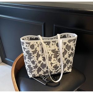 Detailweergave van modieuze draagtas met koeienprint en luxe witte lederen schouderbanden