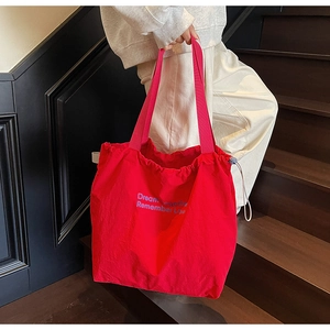 Close-up of red canvas tote bag featuring blue artistic lettering and drawstring closure