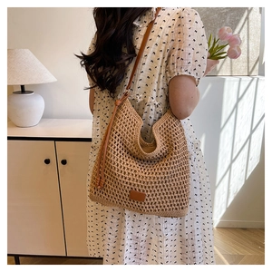 Detail of woven straw tote bag featuring mesh texture and brown leather strap on shoulder
