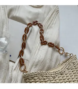 Detail of straw woven bag with acrylic amber link shoulder strap on fabric background