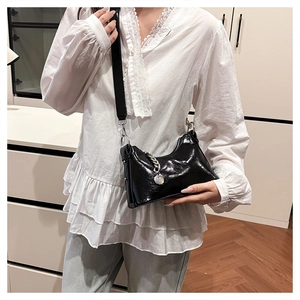 Detail of black glossy leather bag with adjustable wide strap and silver chain accent