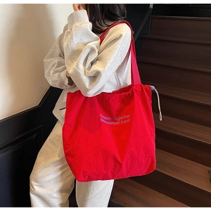 Detail of red nylon tote bag with drawstring closure and printed purple lettering