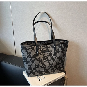Detail van grote shopper met donker abstract patroon en zwarte leren handvatten op een bank