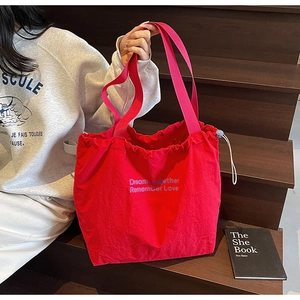 Detail of red drawstring tote bag with blue embroidered text and cord adjustment