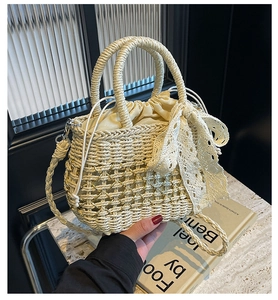 Détail du sac seau en paille avec nœud en dentelle blanche et chaîne dorée