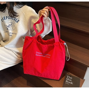 Detail of red drawstring nylon tote bag with pink straps and printed letters