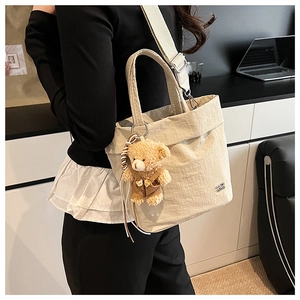 Detail of cream pleated tote bag with wide strap and cute plush bear charm decoration