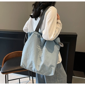 Light blue nylon tote bag with drawstring closure and wide strap shown on model side view