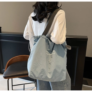 Detail of light blue drawstring tote bag with letter print shown on a model back view