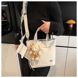 Detail of canvas tote bag with pleated texture, adjustable strap and bear charm