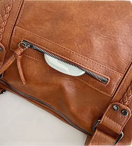 Detail of front zipper pocket with metal rivets and woven texture on brown tote bag