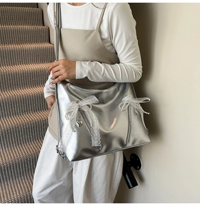 Detail of silver tote bag with lace bow and pearl charms worn over the shoulder