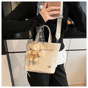Detail of off-white nylon tote bag with metal logo and cute brown teddy bear charm