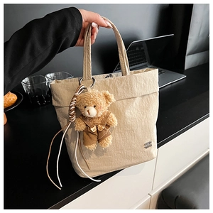 Detail of beige pleated tote bag with a cute brown plush bear charm and soft texture