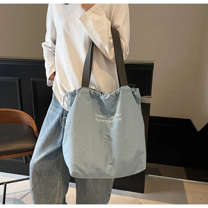 Detail of light blue drawstring tote bag with white art text and wide black shoulder strap