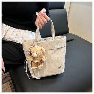 Detail of beige textured tote bag with a cute brown teddy bear pendant on sofa