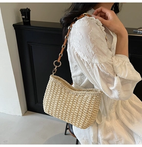 Close-up of beige straw woven underarm bag with gold chain and brown leather strap