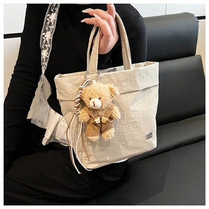 Detailed close-up of a beige canvas tote bag featuring a cute teddy bear charm pendant