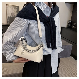 Detail view of cream patent leather crescent bag with bold silver chain and long strap