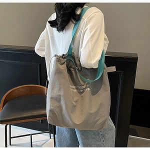 Detail of grey drawstring canvas tote bag with green straps and white printed text