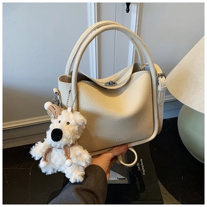 Détail d'un sac à main en cuir grainé blanc crème avec un charmant chien en peluche