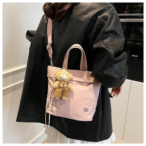 Detail of pink nylon tote bag with teddy bear pendant worn by model on shoulder