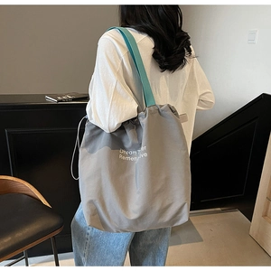 Detail of grey canvas tote bag featuring blue straps and white inspirational lettering