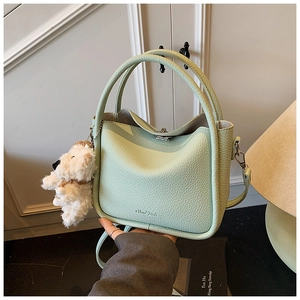 Détail du sac seau en cuir vert clair avec texture litchi et pendentif chien peluche