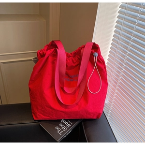 Close-up of red canvas tote bag with pink wide strap and blue drawstring details