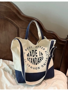 Minimalist canvas tote bag with blue denim stitching on a bed in a home setting