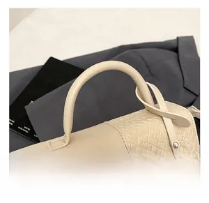 Détail du sac à main beige tissé avec poignée ronde et crochets métalliques