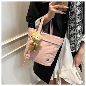 Detail of pink nylon tote bag with plush bear charm and black metal logo plaque