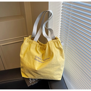 Detail of yellow nylon drawstring tote bag with gray straps on a black seat