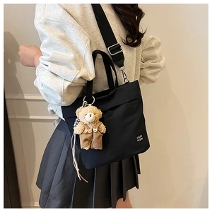 Detail of black canvas tote bag with adjustable strap and cute plush bear charm