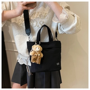 Detail of black canvas tote bag with adjustable strap and cute plush bear charm