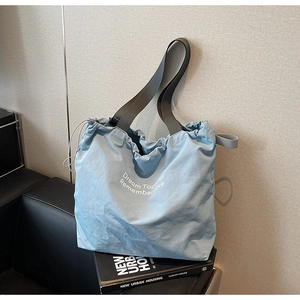 Macro view of light blue nylon tote bag showing drawstring closure and printed text