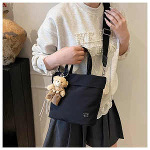 Close-up of black nylon tote bag featuring silver hardware and a cute plush bear charm