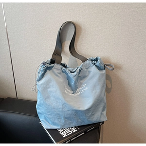 Detail of light blue drawstring tote bag with white inspirational lettering and wide strap