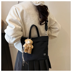 Detail of black canvas tote bag featuring a cute teddy bear plush charm and shoulder strap