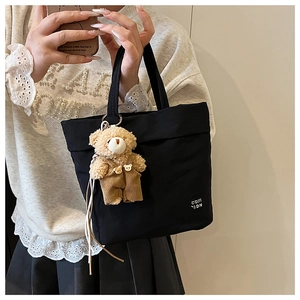 Detail view of a black canvas tote bag featuring a cute teddy bear charm and letter print
