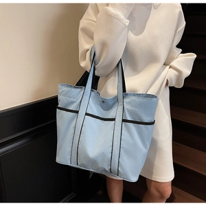 Detail of light blue tote bag with black piping and reinforced handles for daily use