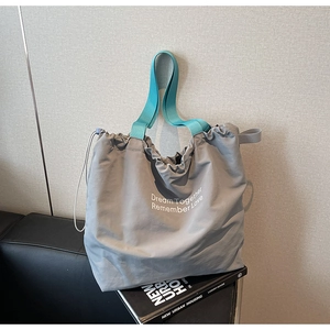 Detail of grey drawstring canvas tote with blue straps and white printed lettering