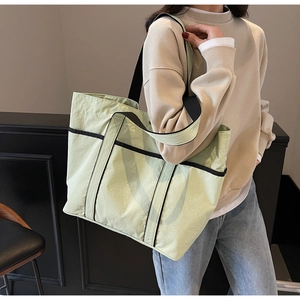Close-up of a large green tote bag with black handles worn on shoulder for commuting